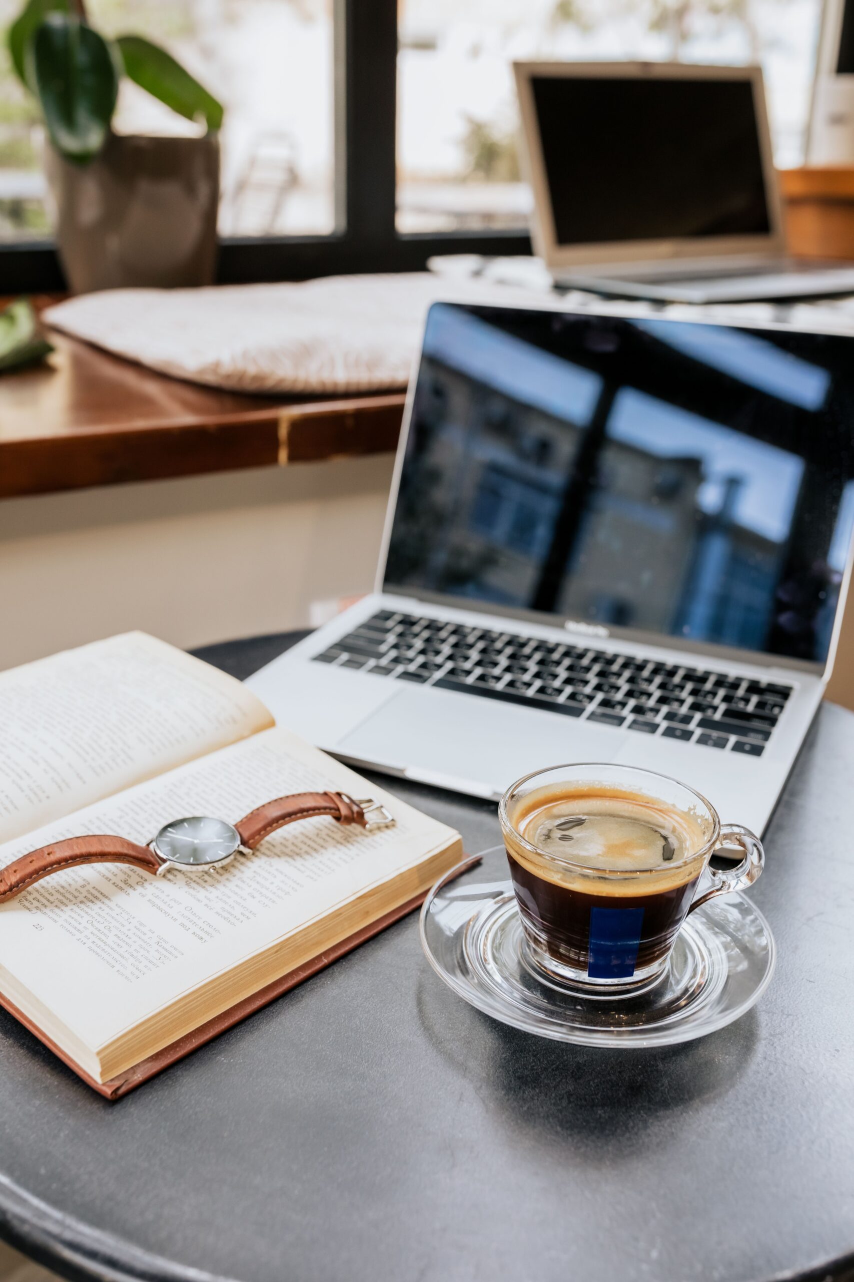 Koffie, laptop en notitieboek op tafel, met horloge erbovenop.